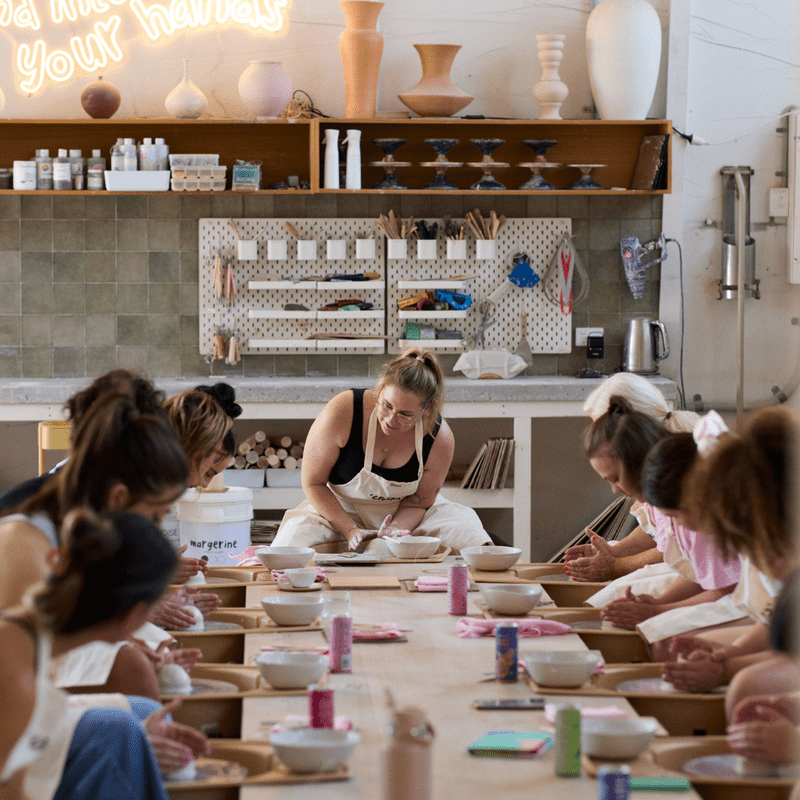 Smiling friends wearing aprons and working with clay at a beginner wheel throwing pottery class at Crockd Studios.