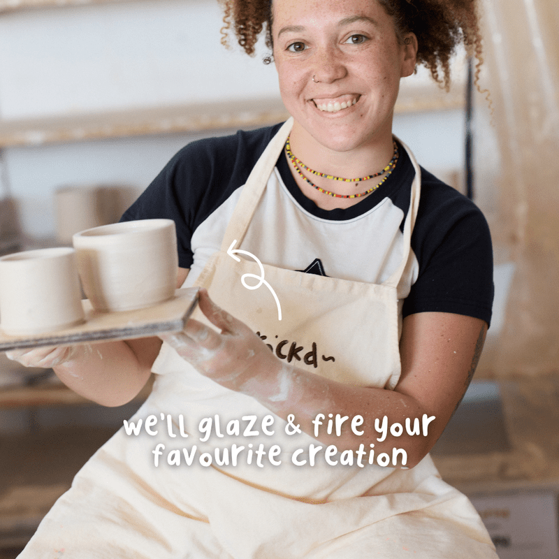Smiling friends wearing aprons and working with clay at a beginner wheel throwing pottery class at Crockd Studios.